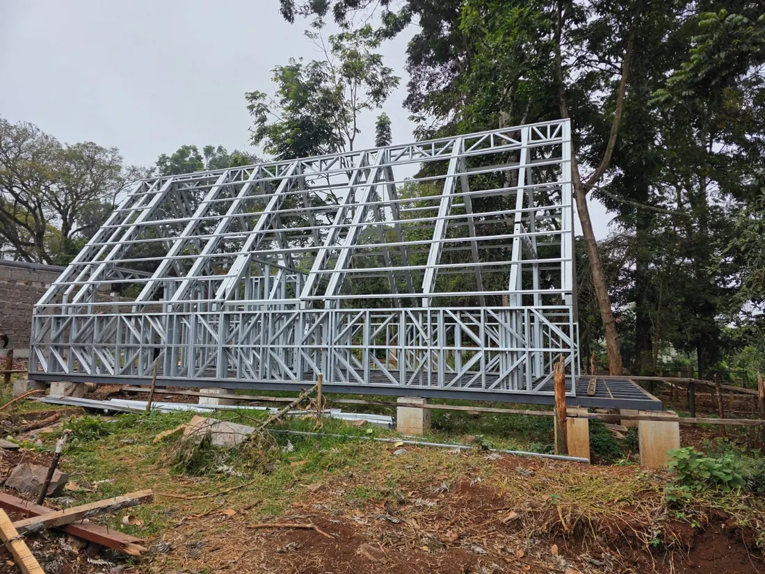 A steel A-frame structure erected on a raised platform among mature trees, its triangular
frames braced and standing ready for cladding